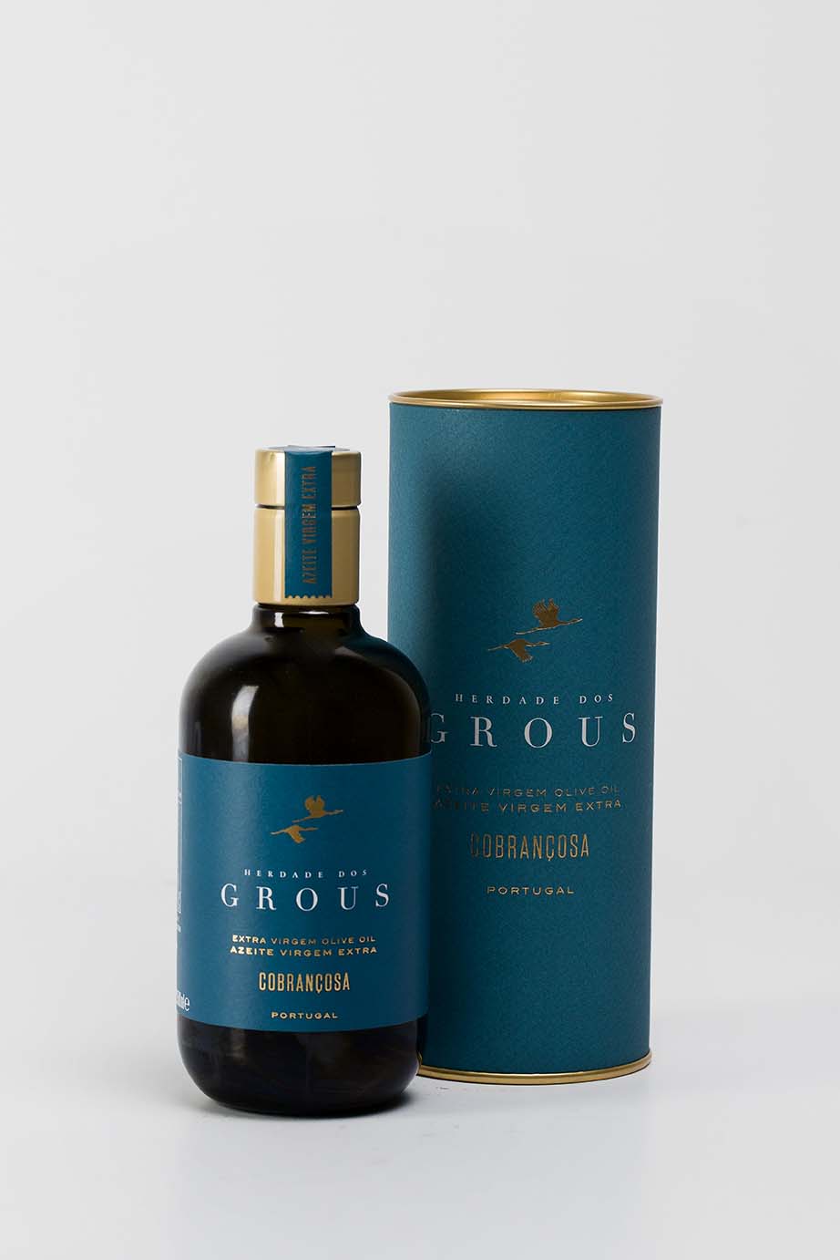 A bottle of olive oil with a blue label and a gold-colored cap, next to its cylindrical blue packaging box, both featuring the brand 'Grous'.